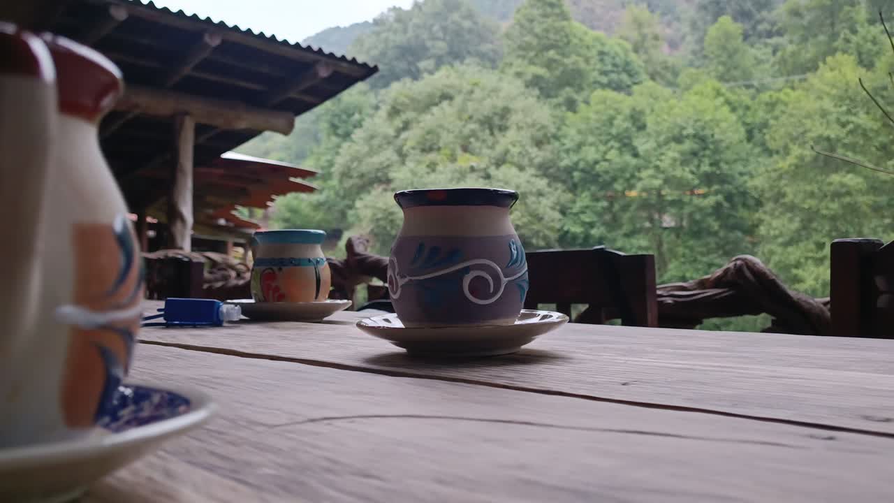 Ceramic cups on a rustic table with a peaceful forest view in the background