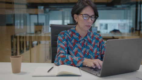 mature businesswoman working on laptop and taking notes at desk