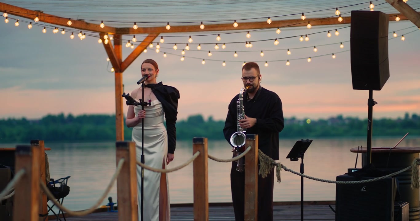 Female Singer and Saxophonist Performing on a Lakeside Pier at Sunset