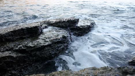 Waves-crashing-into-rocks-near-Budva-old-town-on-the-coastline-of-Montenegro-on-the-Adriatic-coastline-on-a-sunny-sunset-afternoon