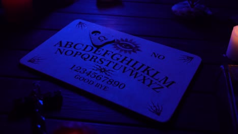close up video of a wooden ouija board on a table surrounded by candles and a cross in a muffed - close up video of a wooden ouija board on a table. wax candles and a cross around. the planchette is slowly moving across the board, spelling out words and numbers. creative mystical content
