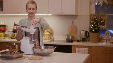 woman works in kitchen and grinds meat in meat grinder