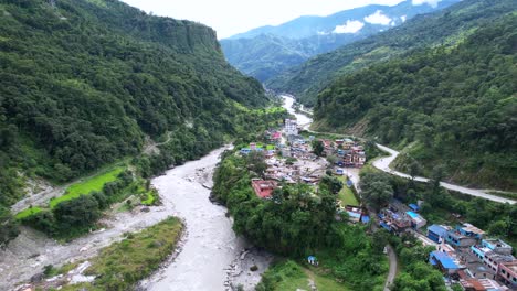 exotic aerial rural scene of gandaki river and green trees on the mountainside, drone flying forward above marpha village in nepal