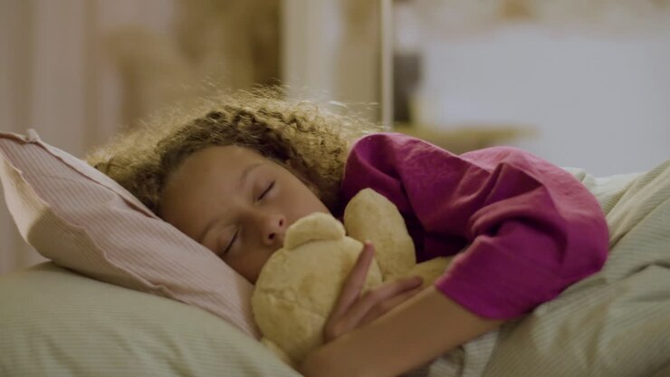 Niña adorable durmiendo en la cama abrazando un peluche