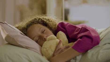 linda niña durmiendo en la cama sosteniendo un juguete suave