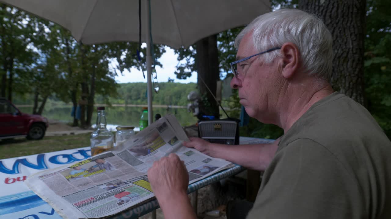 hombre de cabello gris se sienta al aire libre en la escena del bosque leyendo el periódico local