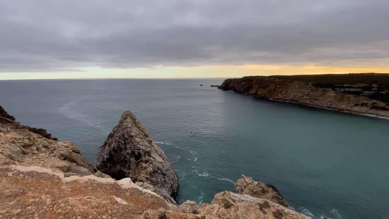 Majestic red cliffs meet the calm Atlantic under a dramatic cloudy sky, showing Sagres’ wild power