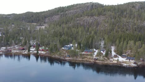 montaña con lago natural forestal y casas pequeñas filmadas con drones en invierno en noruega