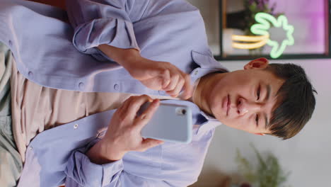 Asian-chinese-adult-man-sitting-on-sofa,-using-smartphone-share-messages-on-social-media-application