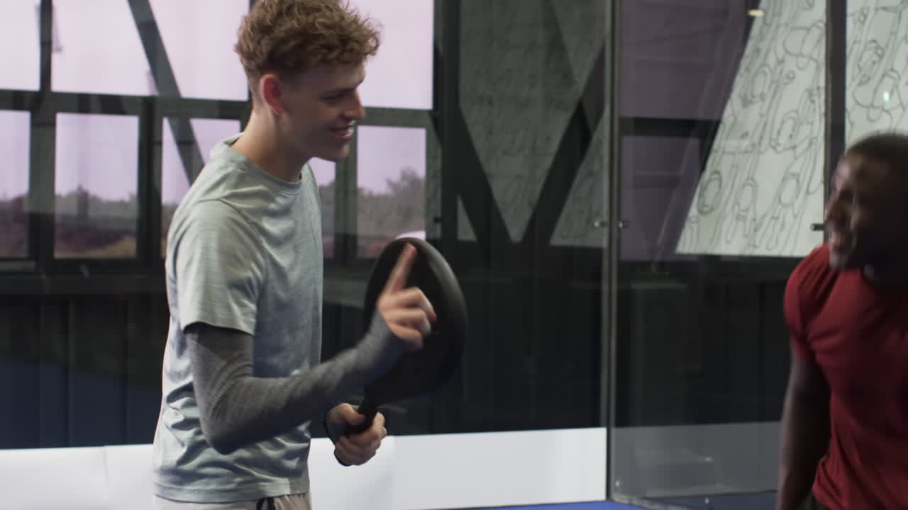 African American man playing padel tennis, holding racket and ball, smiling indoors, at indoor court