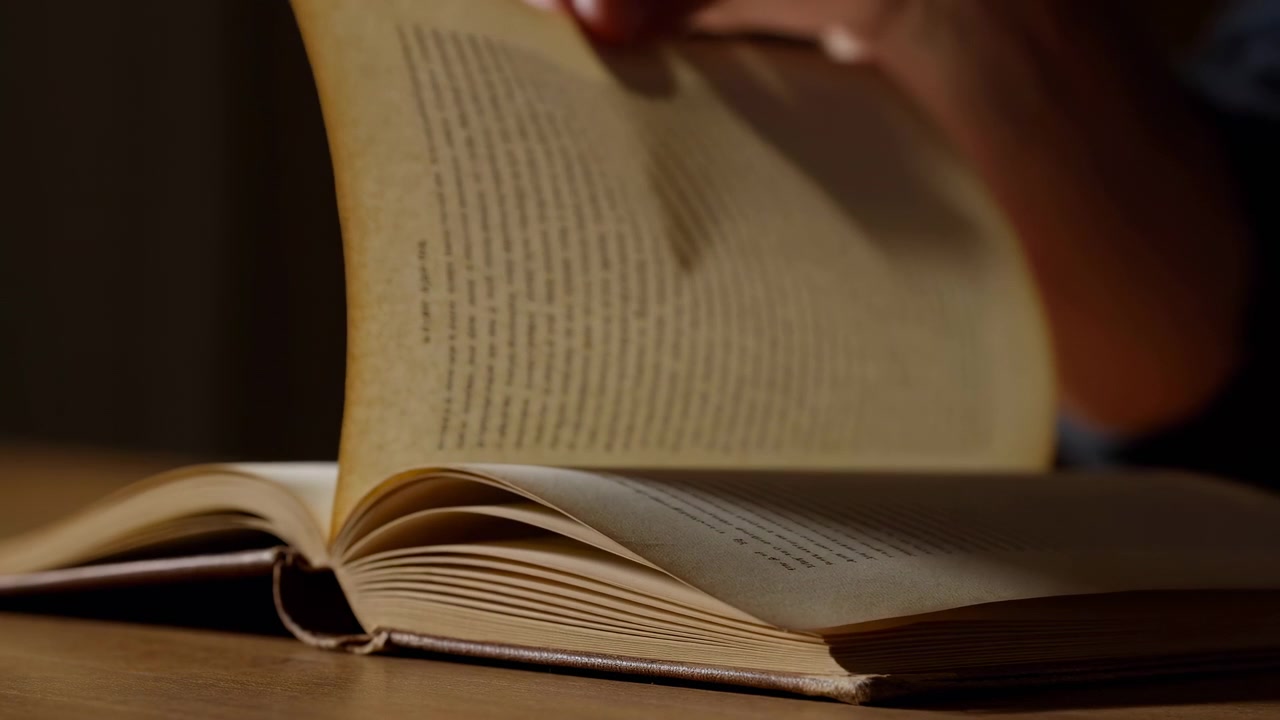 Tavolo scarsamente illuminato, libro aperto con pagine girate a mano, primo piano di carta invecchiata e dorso, texture tattile e calda