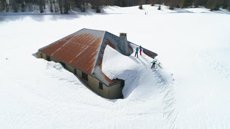 Gruppe-Von-Menschen,-Die-Auf-Dem-Dach-Eines-Verschneiten-Hauses-Klettern-Und-In-Den-Französischen-Bergen-Skifahren