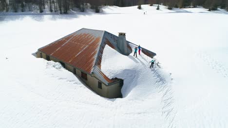 group of people climbing on roof of snowy house and skiing down in france mountains