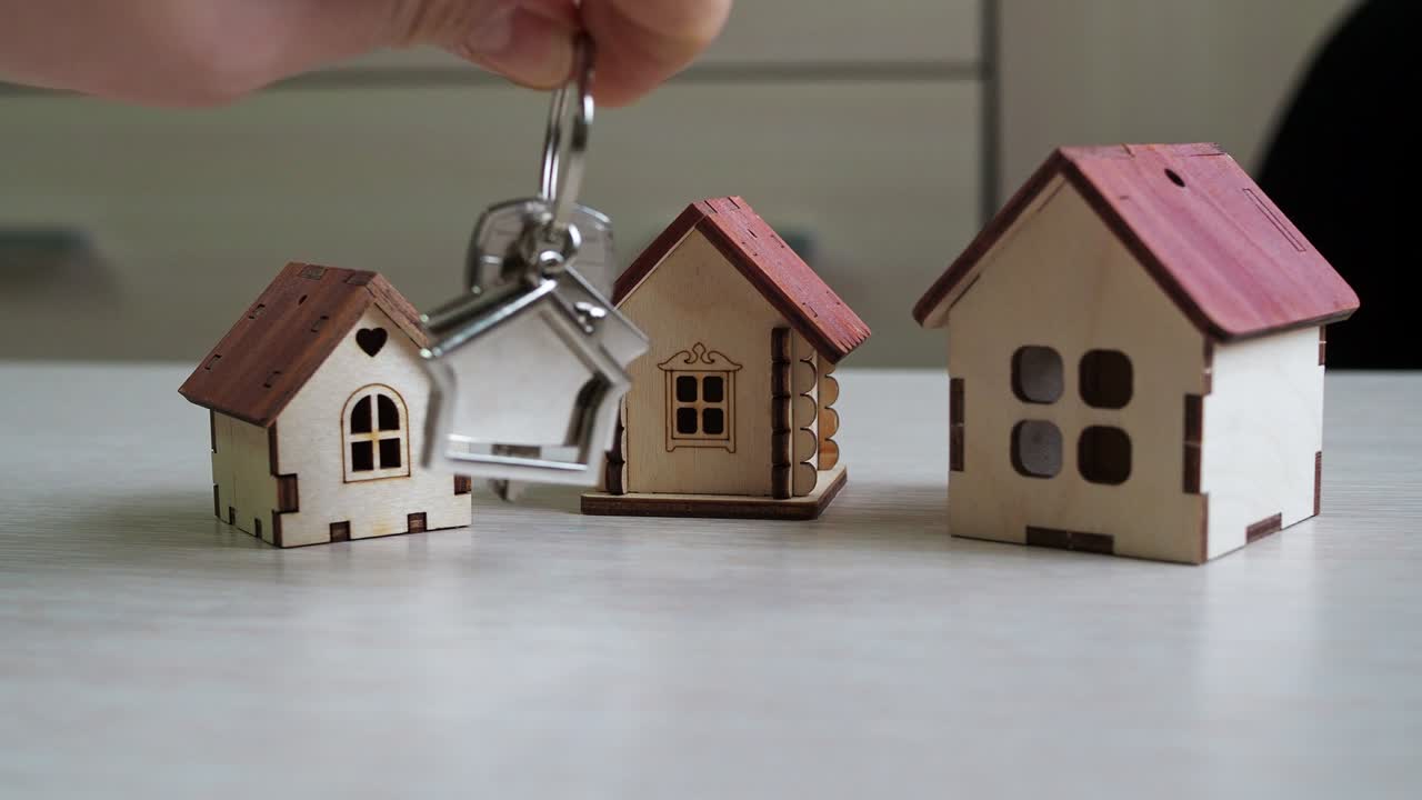집 열를 손에 들고 있는 키체인. 테이블 위에 장난감 집. 부동산 구매. 부동산은 거래