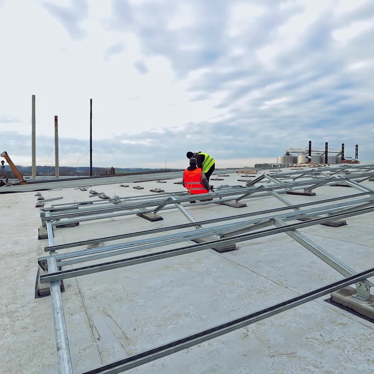 Future solar energy farm on a flat roof. Two workers in protective uniform installing metal basis for putting photovoltaic panels.