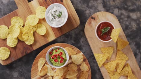 close up view of variety of chips and sauces on wooden trays on black surface