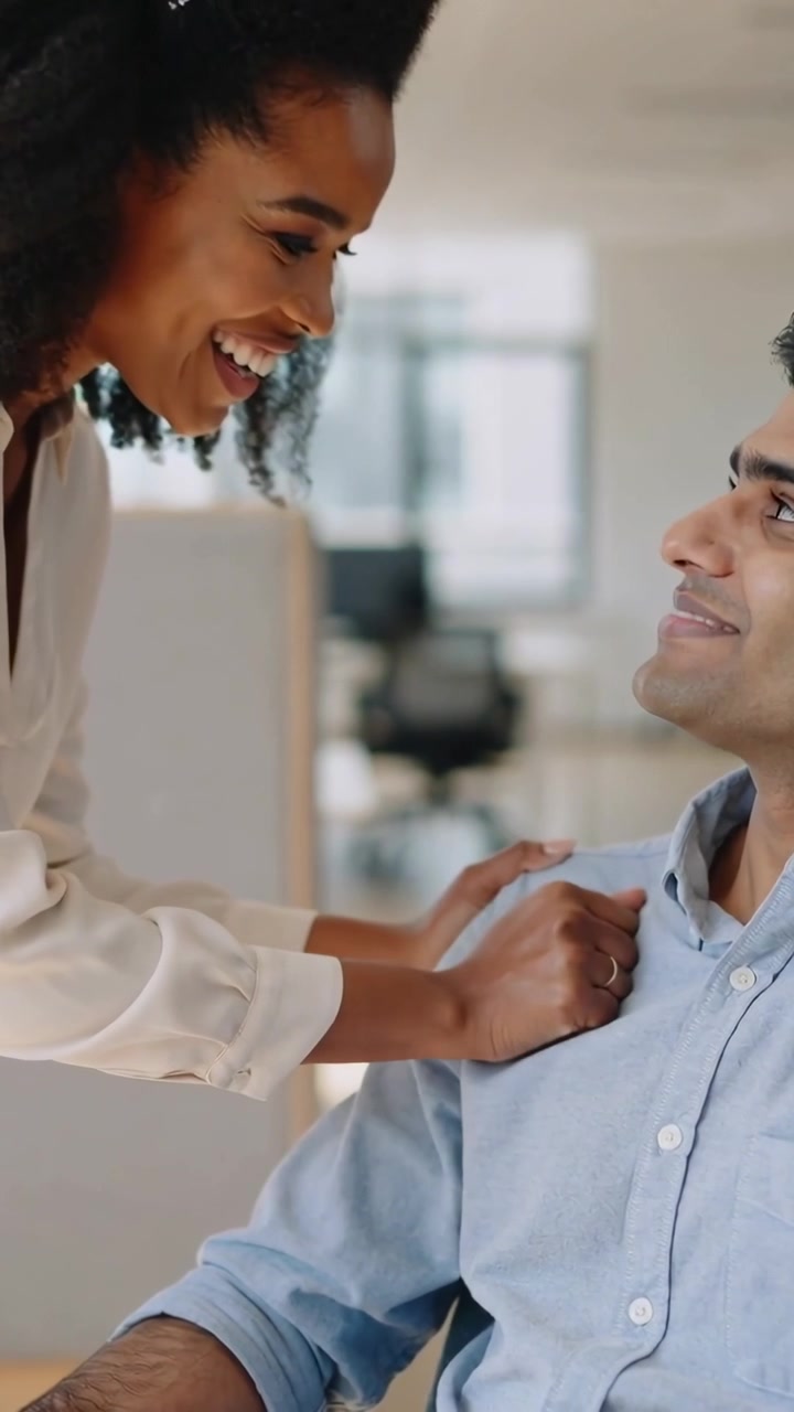 Video verticale: Donna che si china per sistemare il colletto della camicia blu di un uomo in ufficio, lisciando il tessuto.