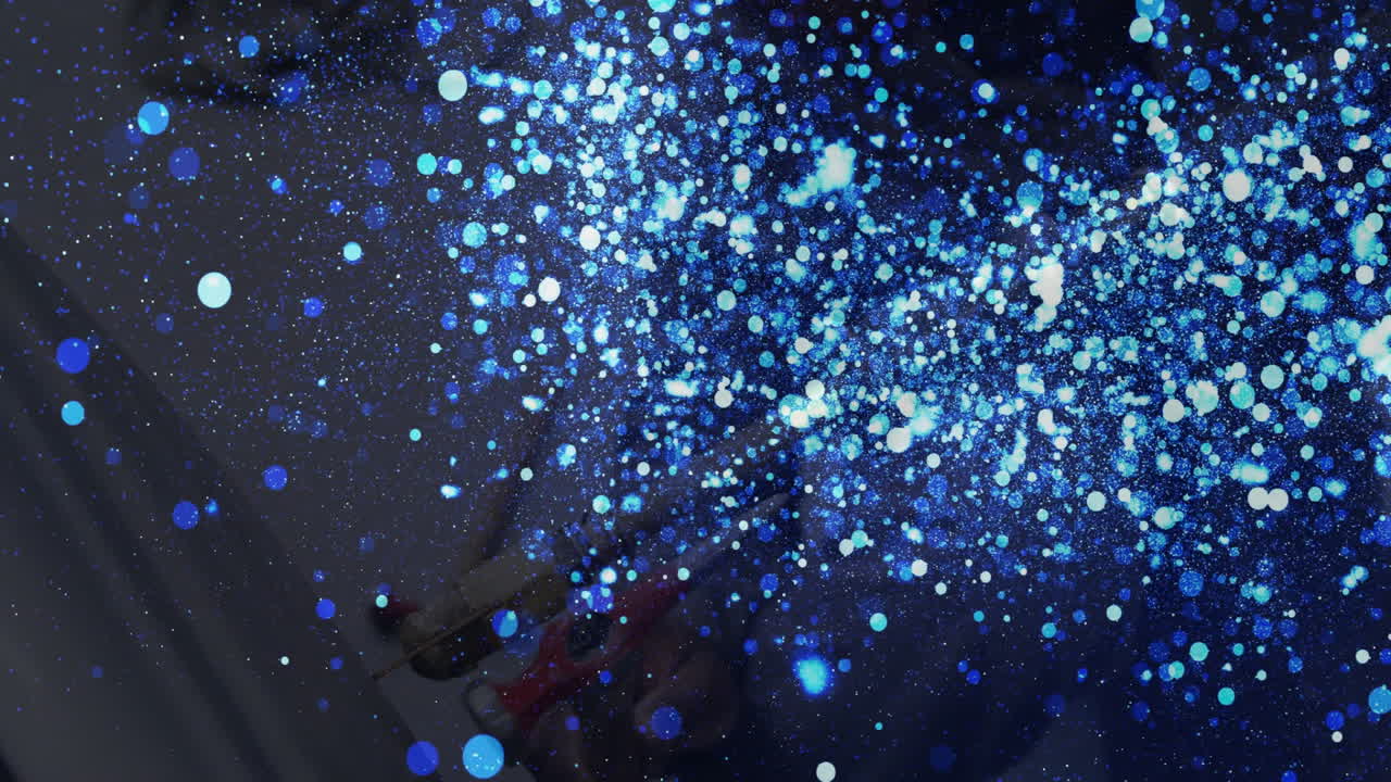 Technician gloved hand handling spray gun in industrial workshop, creating blue particle cloud