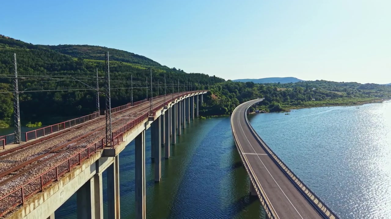 Vista de uma ponte com ferrovia e estrada junto à água sob um céu claro no campo durante o dia.