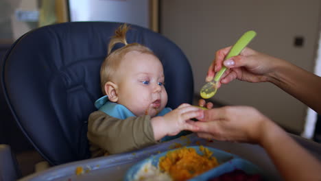 mom's hand is holding an avocado half and scrubbing it with spoon. giving fresh fruit and vegetables to a baby.