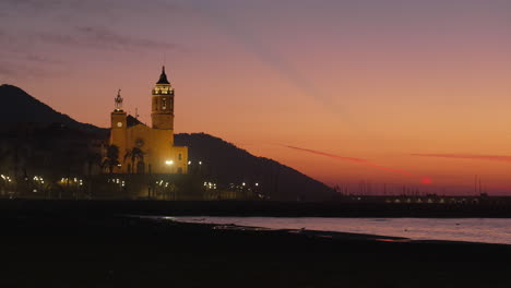 Puesta-De-Sol-Roja-Costa-Del-Mar-Crepuscular-Con-Una-Silueta-De-Iglesia-De-Colinas-Y-Pájaros-Volando