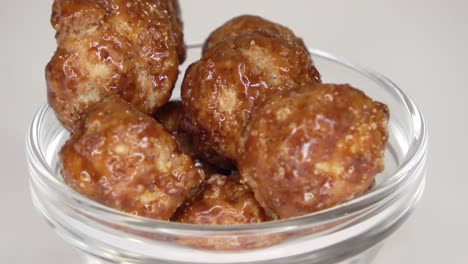 imágenes en bucle de muchas nueces de macadamia confitadas girando en un pequeño cuenco contra un fondo blanco.