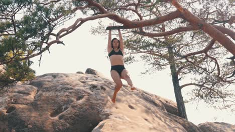 mujer se balancea, se aferra a la rama de un árbol con sus manos vista con el cielo del amanecer en el paisaje rocoso.