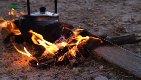 Bright-orange-flames-heating-an-old-tea-urn,-outdoor-sunset,-slow-motion