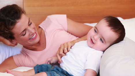 Madre-Feliz-Haciéndole-Cosquillas-A-Su-Hijo-En-La-Cama