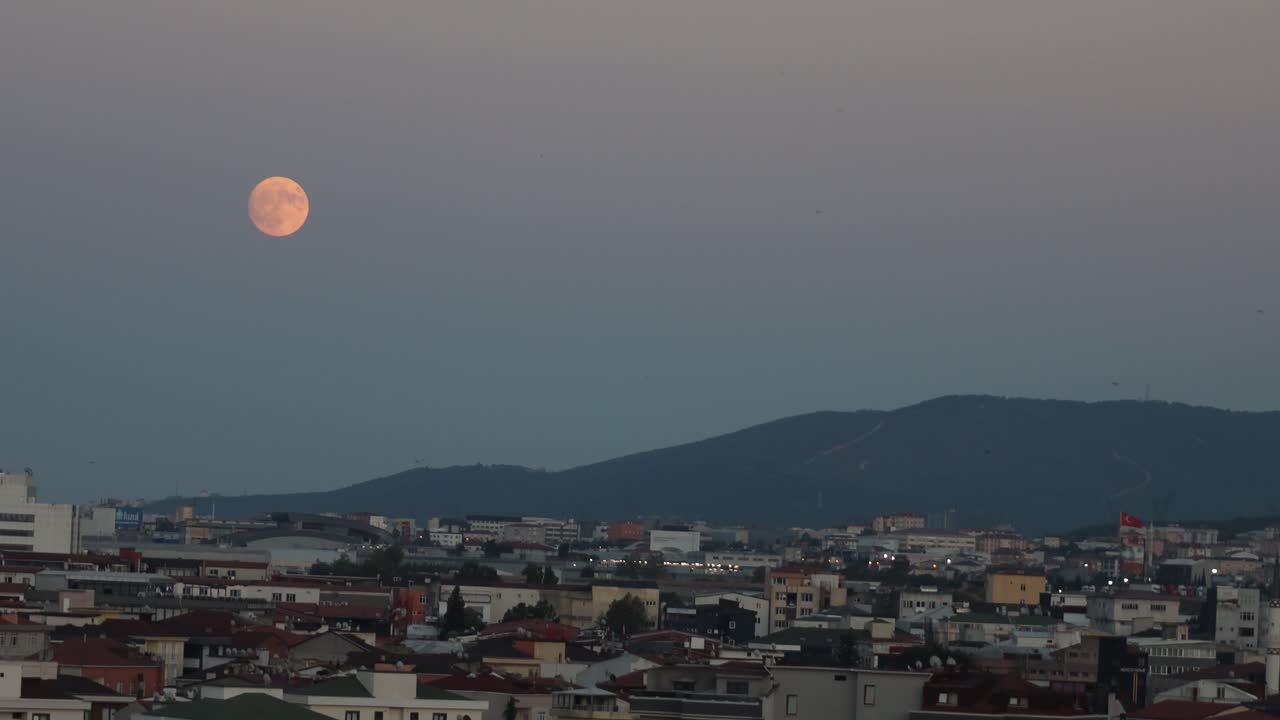 Warm harvest orange red moon rises above Istanbul Turkey hillside as lights flicker on