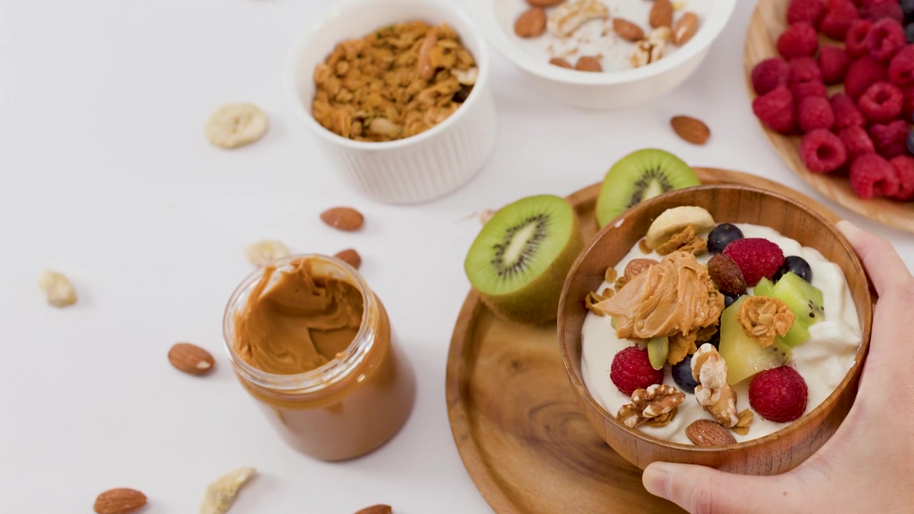 Overhead zoom out reveals a wooden bowl filled with yogurt, fruit, and nut butter.