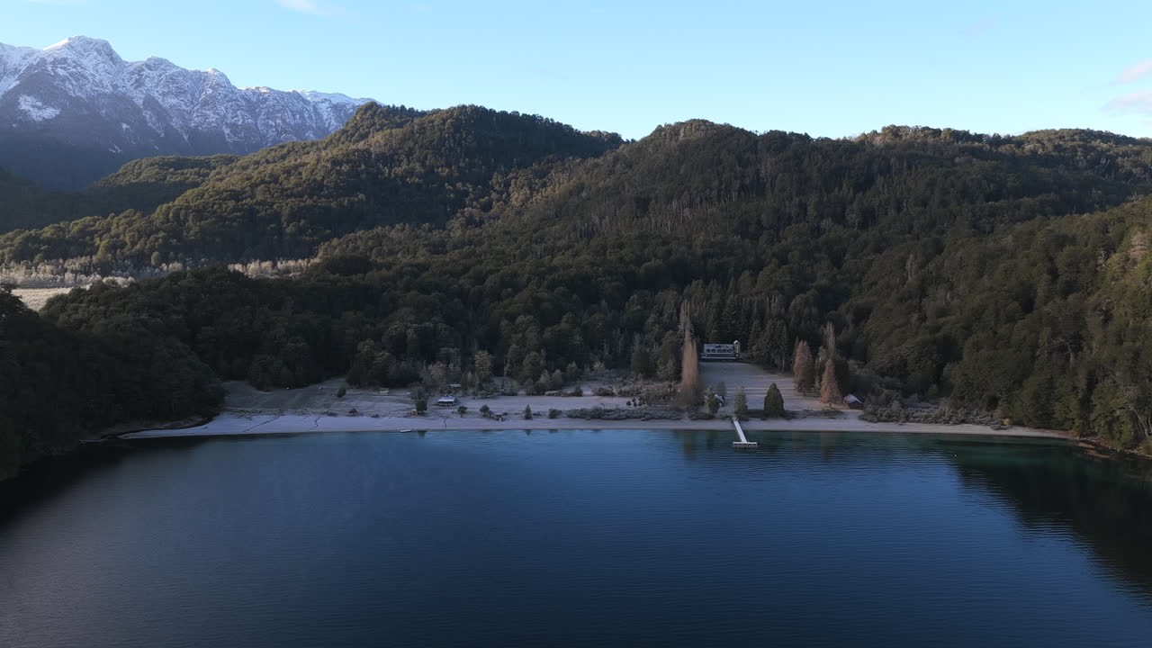 Letecký pohled z dronu přibližující se k pláži Lago Espejo s lesem a zasněženými Andami v Patagonii.