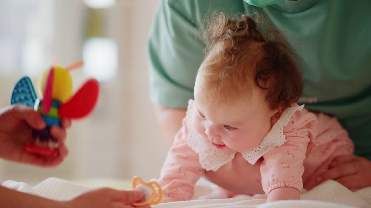 Baby lying on the stomach and focusing on a colorful toy held by an adult during a developmental activity