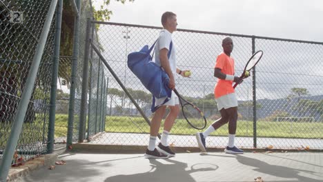 rear view of diverse male tennis players walking and talking at outdoor court in slow motion