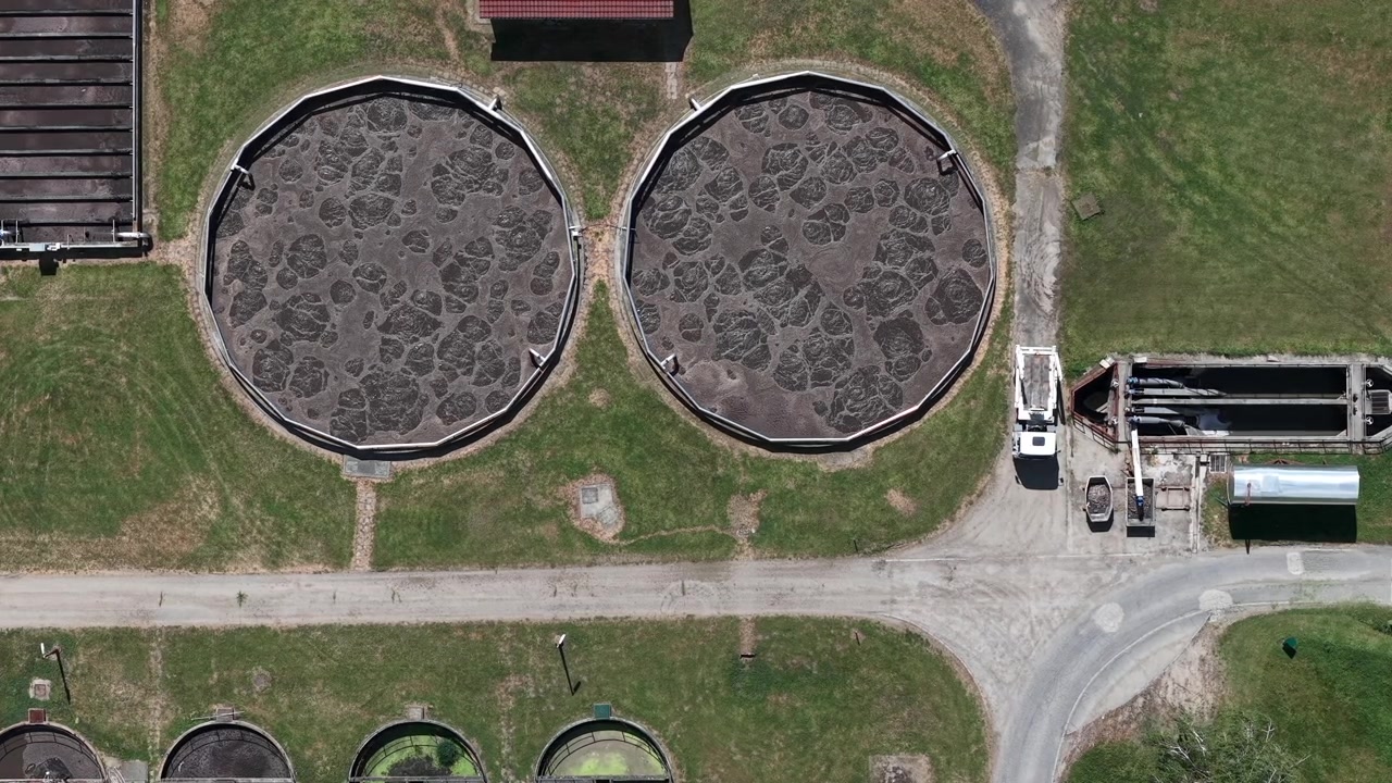 An aerial perspective of a wastewater treatment facility showcases large circular tanks with churning water and industrial infrastructure.