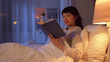 Mujer-Asiática-Joven-Leyendo-Un-Libro-En-La-Cama-En-Casa.-Gente,-Hora-De-Dormir-Y-Concepto-De-Descanso-Mujer-Asiática-Joven-Sonriente-Feliz-Leyendo-Un-Libro-En-La-Cama-En-Casa-Por-La-Noche