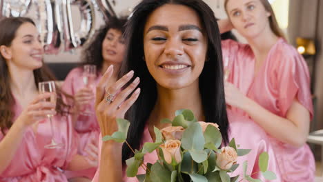 woman holding bouquet, wearing pink silk nightdress, smiling while touching her hair and looking at camera