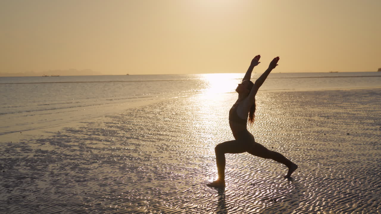Donna che pratica la posizione del guerriero yoga sulla spiaggia al tramonto