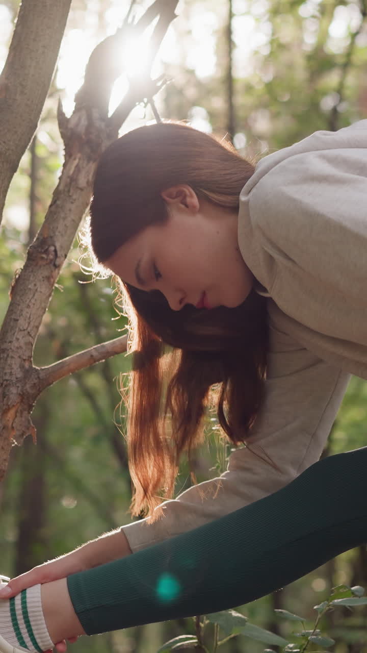 숲에서 조을 한 후 가지에 다리를 는 여성. 건강한 스포츠 의류를 입은 여성이 밀집한 숲에 둘러싸인 여름날에 활발한 생활 스타일 훈련을 즐긴다.