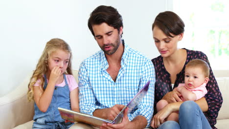 familia linda sentada en un sofá y mirando un libro juntos