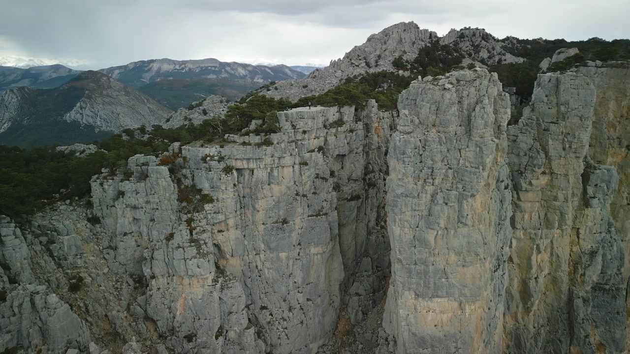 Drone shot of Cadières de Brandis in France. The mountain's rock formations drop steeply into the depths. In the background, the view opens up to the mountainous horizon.