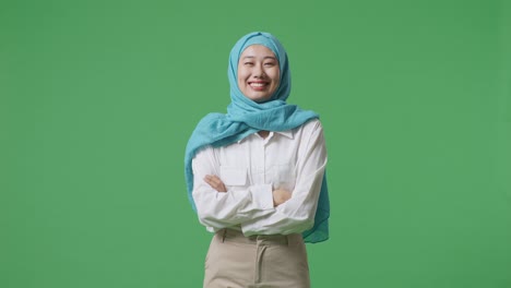 mujer musulmana sonriendo y cruzando los brazos mientras está de pie en el estudio de fondo de la pantalla verde