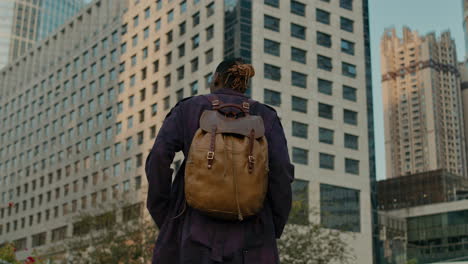 black man exploring big city with backpack, view from behind