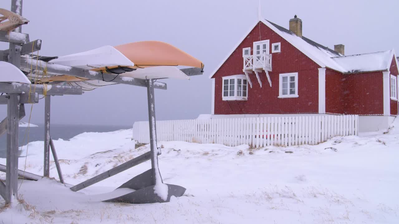 Slow motion video of canoes in front of a red house on the coast in a snowstorm