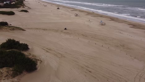 Aerial-tracking-shot-of-quad-bike-driving-on-sandy-beach-leaving-after-trip-during-sunny-day