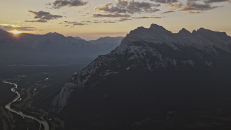 Banff-AB-Canada-Aerial-v9-high-altitude-drone-flyover-capturing-Bow-river,-forested-valley-and-golden-glowing-sun-peeking-behind-the-mountain-ranges---Shot-with-Mavic-3-Pro-Cine---July-2023