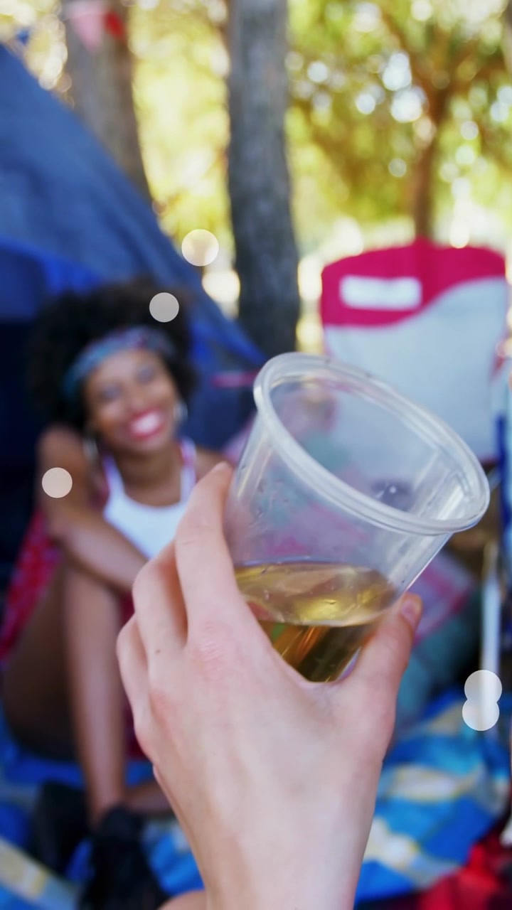 Vertical video: Front woman moving cup and talking at picnic event, causing focus, bokeh and smiles