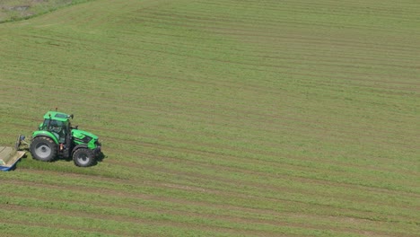 green tractor cutting grass in large field, creating neat parallel rows, drone shot.