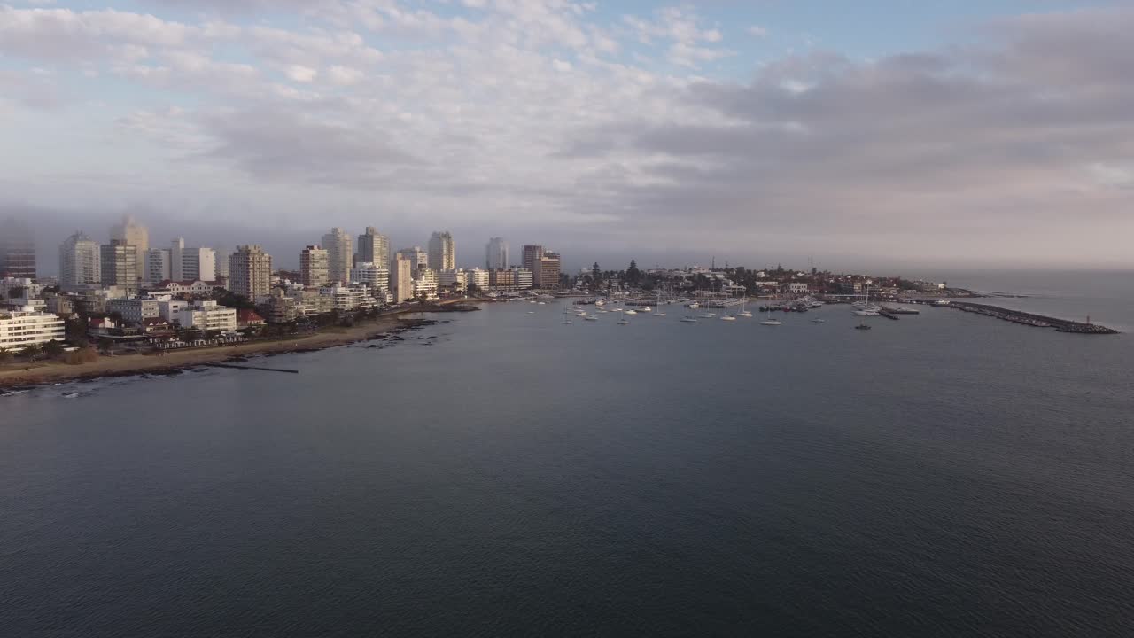 toma panorámica aérea de la ciudad de punta del este con playa de arena, horizonte y puerto con barcos