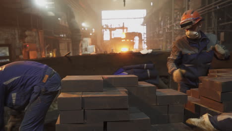 metal workers handling molten material bricks in a factory